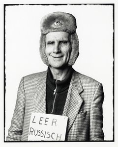 108335 Portret van een man (P. Ernst, bijgenaamd De Rus ) met een bontmuts op en een bordje leer russisch om zijn nek.